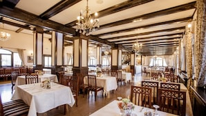 Un comedor amplio con varias mesas y sillas, vigas de madera en el techo y candelabros.