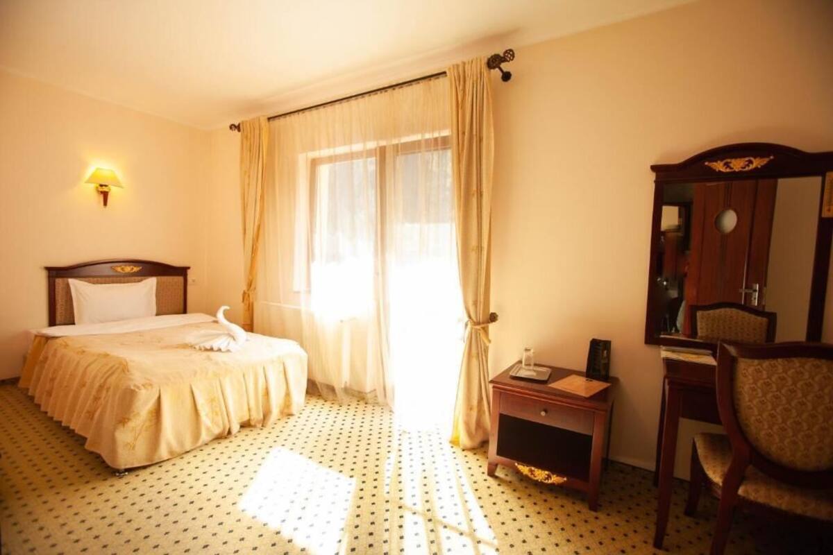 A hotel room with a bed, a desk, a chair, a mirror, and a window with curtains.