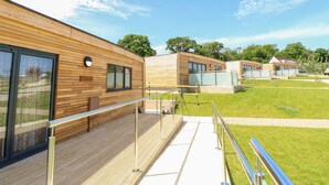 A modern building with wooden paneling and large windows, a covered outdoor area with a metal railing, and a grassy courtyard. - Champagne (Ryde)