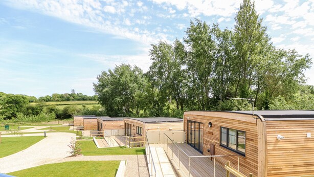 A row of modern, wooden cabins with large windows and a deck area, set in a lush, green landscape. - Cava (Ryde)