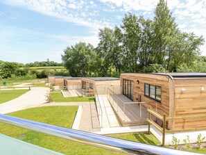 Une rangée de chalets modernes en bois, dotés de grandes fenêtres et d’une terrasse, nichée dans un paysage luxuriant et verdoyant.