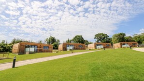 A row of modern, wooden cabins with large windows, set on a grassy slope under a partly cloudy sky. - Cava (Ryde)