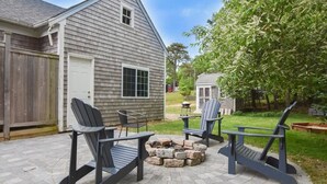 Un jardin avec un foyer, des fauteuils Adirondack et une terrasse en bois.