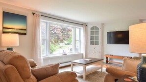 Un salon avec un canapé, une table basse, un téléviseur et une fenêtre donnant sur des arbres.