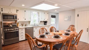 Une cuisine avec des meubles blancs, une cuisinière, un four à micro-ondes et une table à manger pour six personnes, avec des chaises.