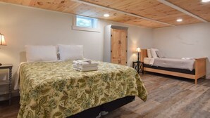 Une chambre avec un plafond en bois, un lit recouvert d’une couvre-lit à motifs floraux, un plus petit lit, une table de chevet et une fenêtre.