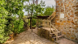 Un escalier en pierre mène à une terrasse en bois agrémentée d’une pergola, le tout étant entouré d’une végétation luxuriante.
