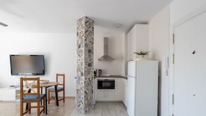 A compact kitchen with a TV, dining table, chairs, and a refrigerator.