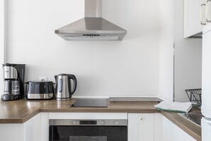 Une cuisine moderne équipée d’une hotte en acier inoxydable, d’une machine à café, d’une bouilloire et d’un grille-pain, le tout posé sur le plan de travail.