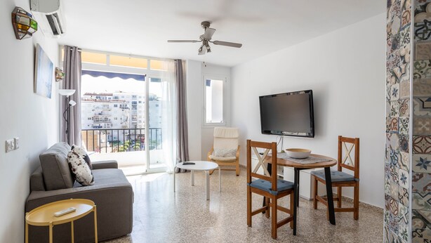 A modern living room with a sofa, a TV, a ceiling fan, and a balcony with a view of the city.