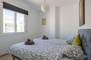 Une chambre à coucher avec un grand lit, deux oreillers, une œuvre d’art accrochée au mur et une fenêtre avec des stores.