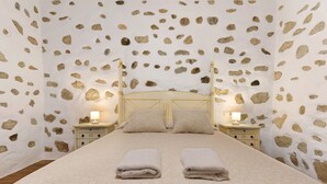 Habitació amb llit, dues taules de nit amb làmpades i una paret amb motius de pedra.