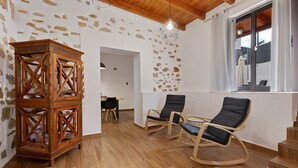 Habitació amb terra de fusta, paret de pedra, taula de fusta, dues cadires bressol i un llum penjant.