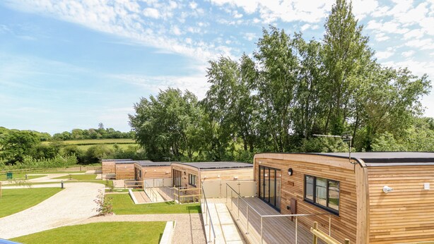 Una hilera de cabañas modernas de madera con amplios ventanales, un camino de grava y una zona ajardinada.