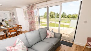 Una sala moderna con un sofá gris, dos cojines estampados, un comedor con mobiliario de madera y un amplio ventanal corredero que da a un patio exterior.