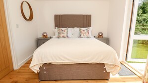 Une chambre à coucher avec un lit, des tables de chevet, un miroir rond et une vue sur la verdure.