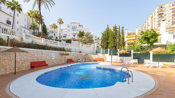 A swimming pool with a stone wall, lounge chairs, and a red bench.