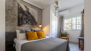 A bedroom with a bed, a nightstand, a chair, a window with curtains, and a painting on the wall.