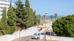 A coastal road with a white car parked by the curb, a no-entry sign, and a building with a tiled roof.