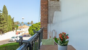 A balcony with a railing, a potted plant, and a view of the street and sea.