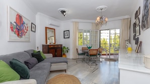 A living room with a sofa, dining table, chairs, and a kitchen area.