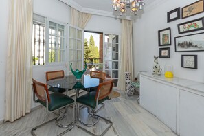Un coin repas comprenant une table en verre, quatre chaises, un lustre et des œuvres d’art accrochées au mur.