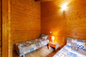 Una habitación tipo cabaña con dos camas de madera, una mesita de noche y una lámpara fijada a la pared.