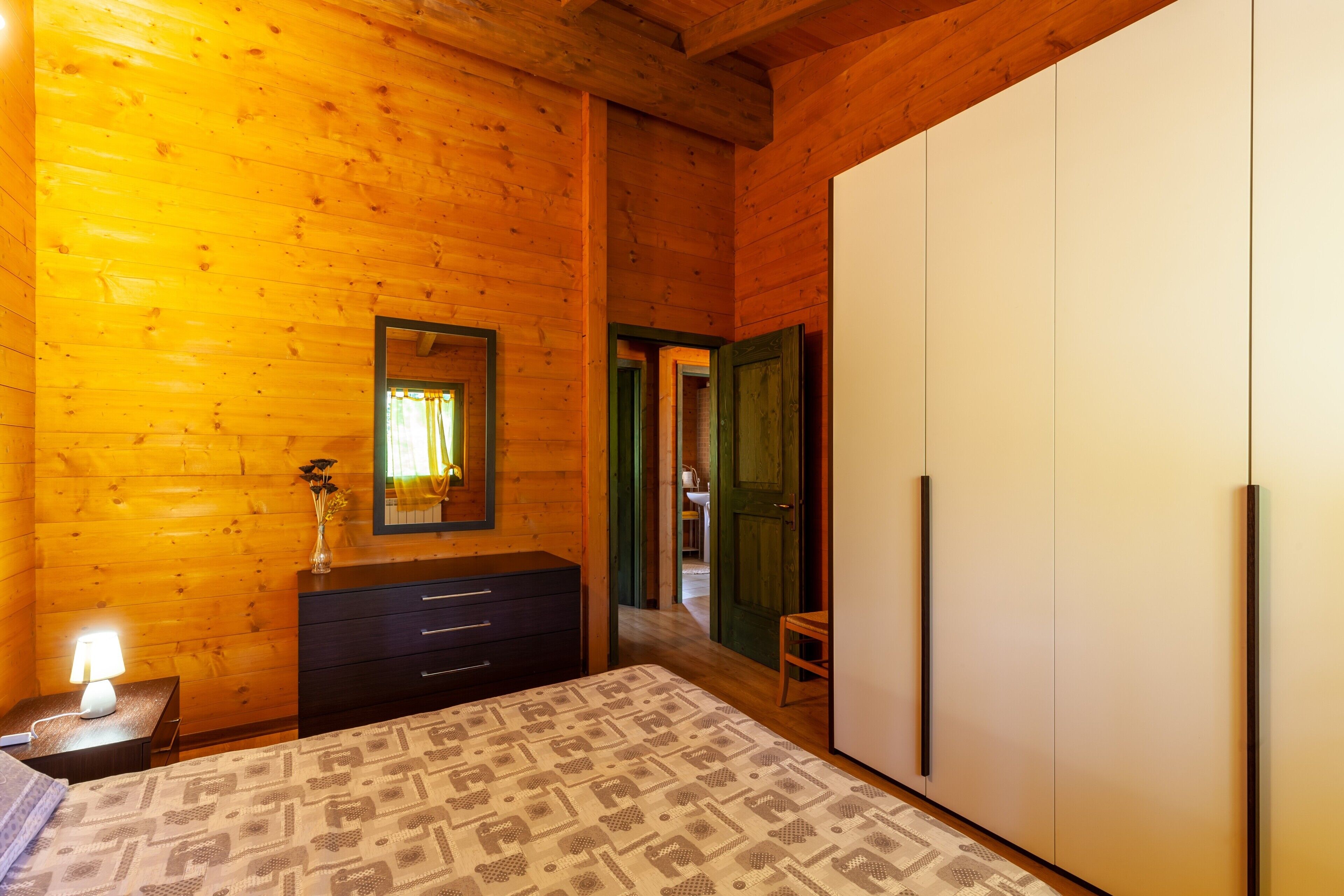 Une pièce en bois comprenant un lit, une commode, un miroir et une armoire.