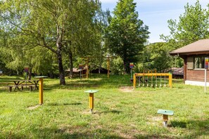 Un parque con mesas de picnic, columpios y un edificio de madera.