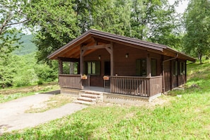 A wooden cabin with a porch, steps leading to the entrance, and a view of the surrounding forest.
