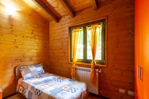 Una habitación de cabaña de madera con cama, una ventana con cortinas y un radiador.