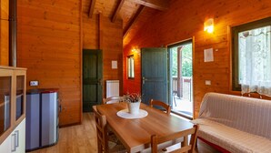A wooden cabin interior with a dining table, chairs, a sofa, and a small refrigerator. - Chalet 'Mirtillo' – Villaggio Anemone with Mountain Views and Private Terrace (Capanne)