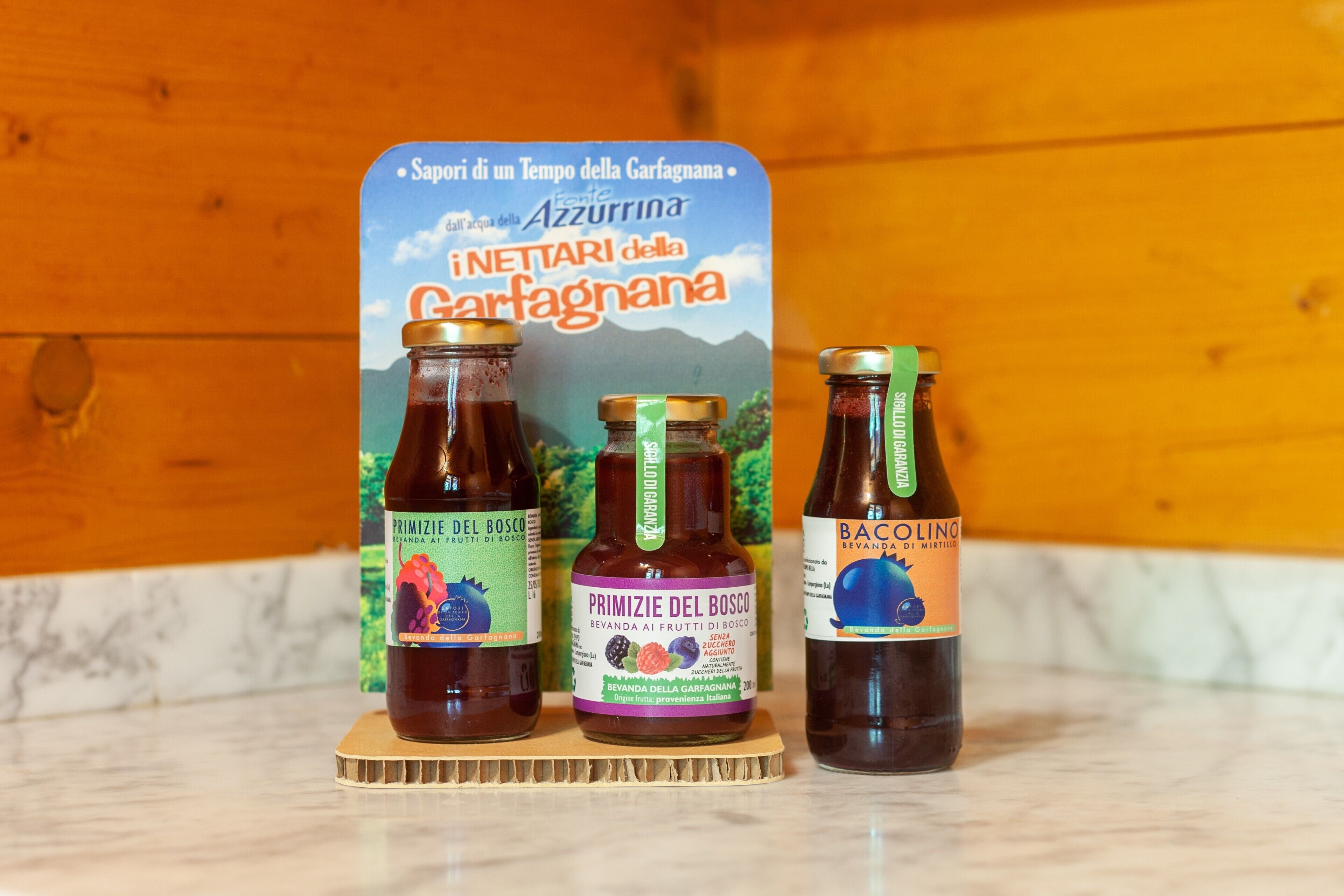 Tres botellas de Primitizie del Bosco sobre una tabla de madera, con un panel de pared de madera y un letrero de fondo.