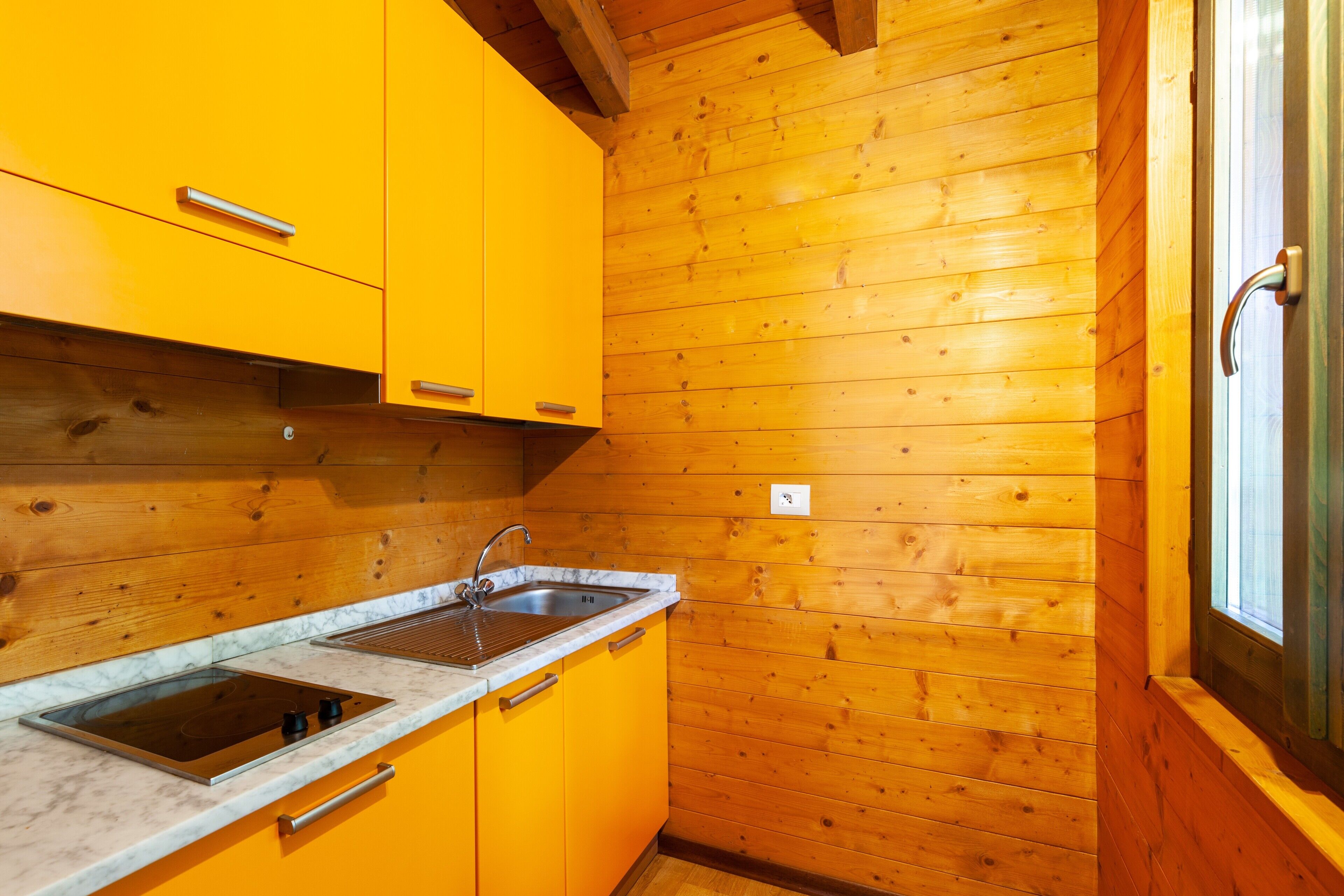 Een kleine keuken met houten wanden, een spoelbak en een ingebouwd fornuis.