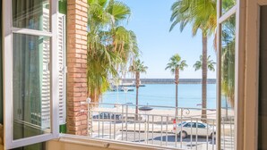 Un balcón con vistas al mar, palmeras y coches estacionados.