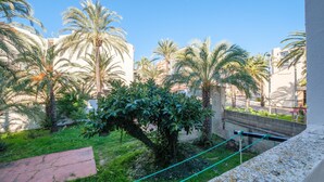 Un patio con palmeras, un banco de piedra y vistas de edificios al fondo.
