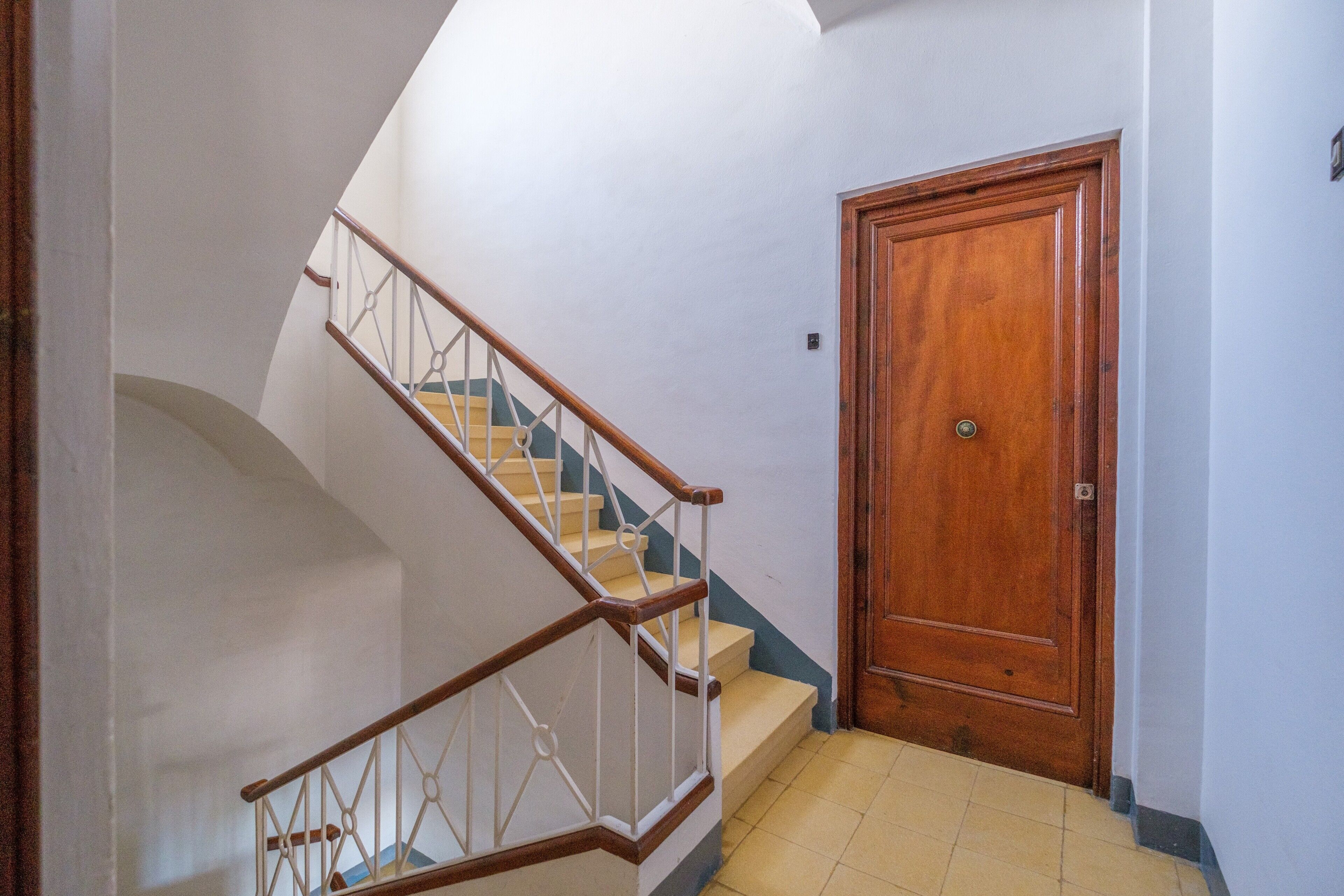 Una escalera con barandilla de madera y peldaños blancos, que lleva a una puerta de madera.