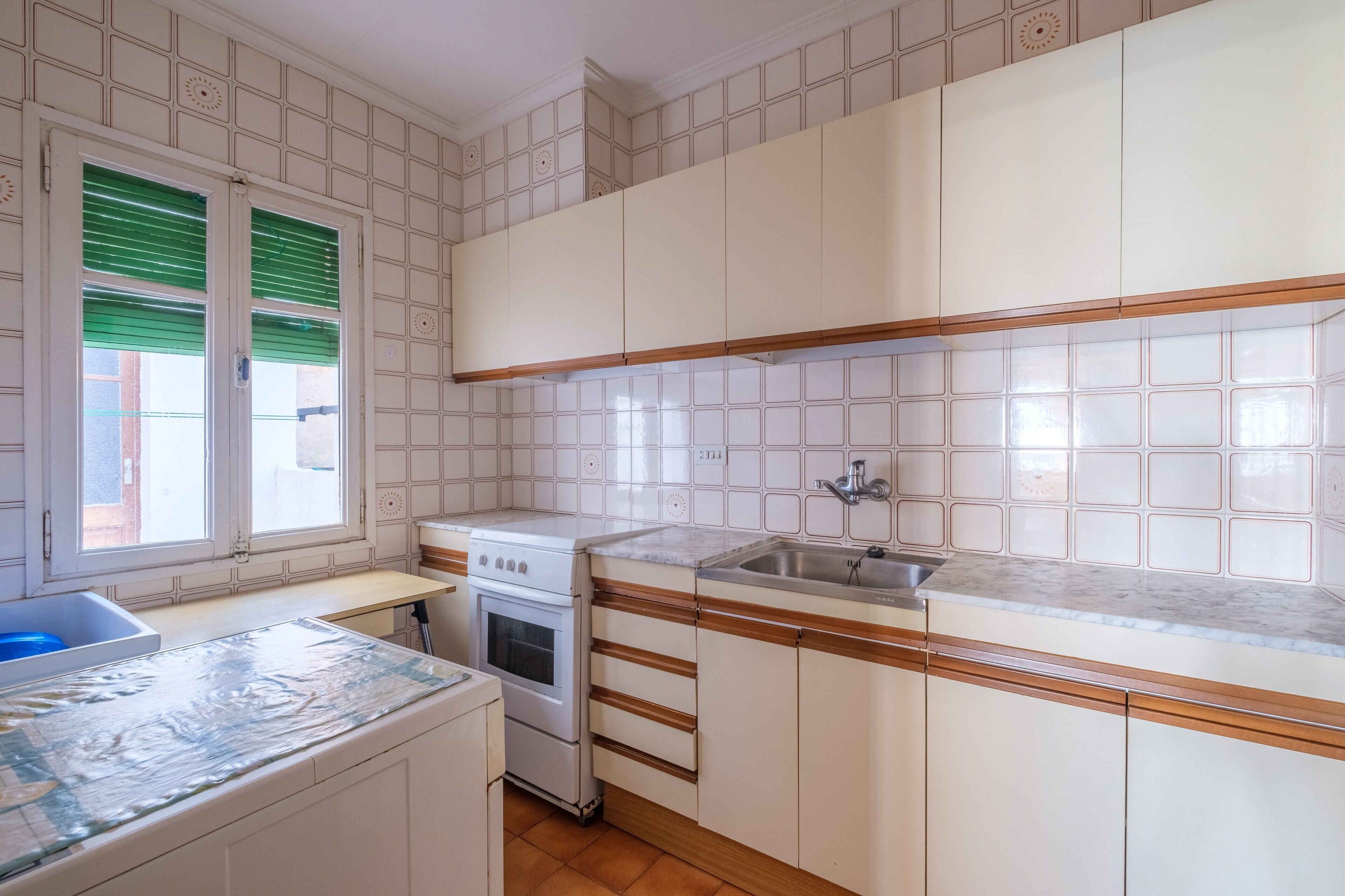 A kitchen with white cabinets, a stove, a sink, and a window with green blinds.