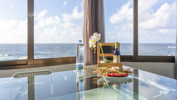 A glass table with a bottle of water, a floral arrangement, and a plate of food. - Apartment 'Casita Independiente Frente al Mar' with Terrace & Wi-Fi (tacoronte)