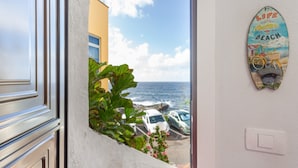 A view from a window overlooking a beach with parked cars and a surfboard decoration on the wall. - Apartment 'Casita Independiente Frente al Mar' with Terrace & Wi-Fi (tacoronte)