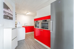 A kitchen with red cabinets, a stainless steel refrigerator, a microwave, and a washing machine.