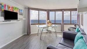 A room with a dining table, chairs, a sofa, a TV, and large windows with a view of the sea. - Apartment 'Casita Independiente Frente al Mar' with Terrace & Wi-Fi (tacoronte)