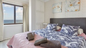 A bedroom with a bed, a window with curtains, a brick wall, and two wall art pieces. - Apartment 'Casita Independiente Frente al Mar' with Terrace & Wi-Fi (tacoronte)