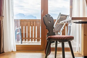 Une chaise en bois dotée d’un siège et d’un dossier rembourrés, placée près d’une fenêtre donnant sur une terrasse en bois et des montagnes.