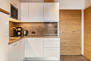 Une cuisine moderne avec des armoires blanches, un four à micro-ondes, une machine à café et une porte en bois.