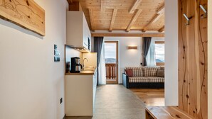 A modern interior with a kitchen, dining area, and living room, featuring wooden beams and a view of the outdoors.