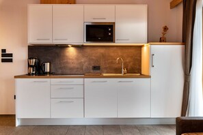 Une cuisine moderne avec des meubles blancs, un four à micro-ondes en acier inoxydable, une machine à café et un évier.