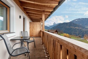 A balcony with a wooden railing, a table, and two chairs, overlooking a mountainous landscape. - Holiday Apartment 'Hatzes Panorama' with Mountain Views, Balconies & Wi-Fi (Lajen)