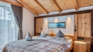 A bedroom with a wooden ceiling, a bed with a plaid bedspread, pillows, and a nightstand.