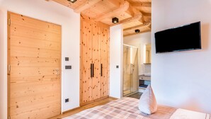 A bedroom with a checkered bedspread, wooden wardrobe, and a mounted TV. - Holiday Apartment 'Hatzes App Raschötz' with Mountain View, Balcony and Wi-Fi (Lajen)